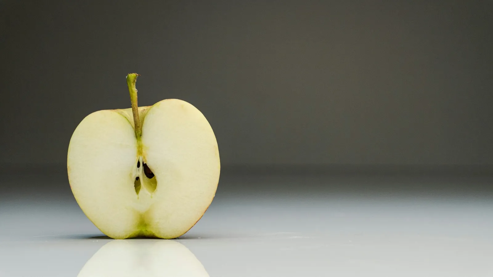 An apple cut in half on a grey surface