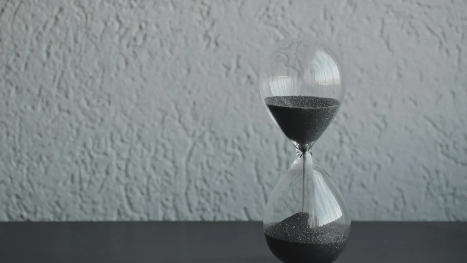An hourglass with sand running through it on a grey surface