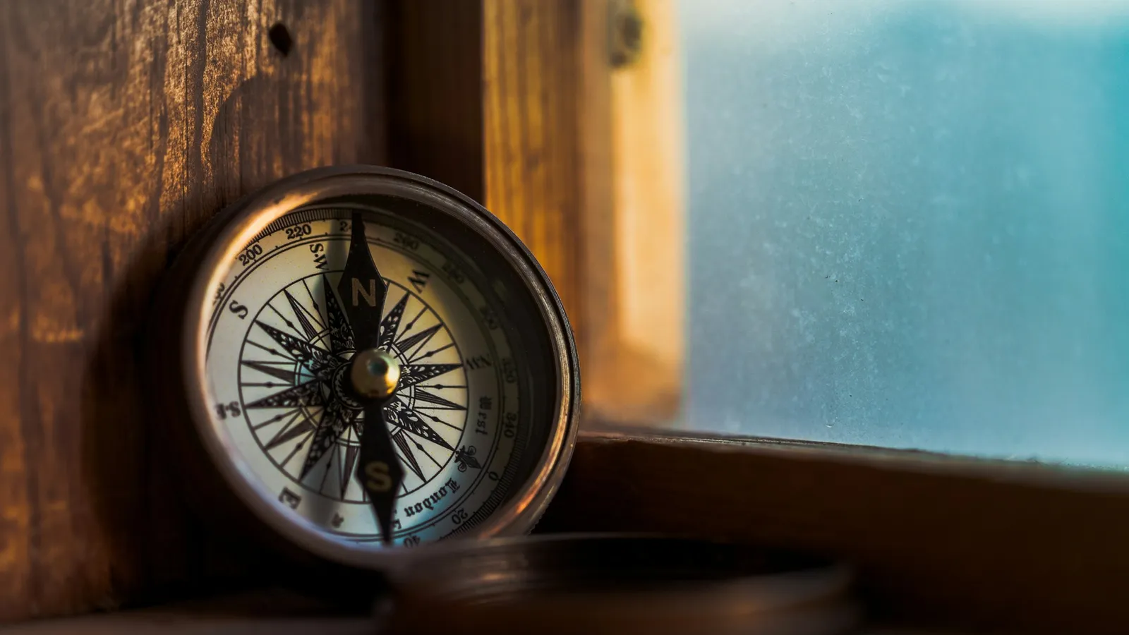An old brass compass on a wooden windowsill