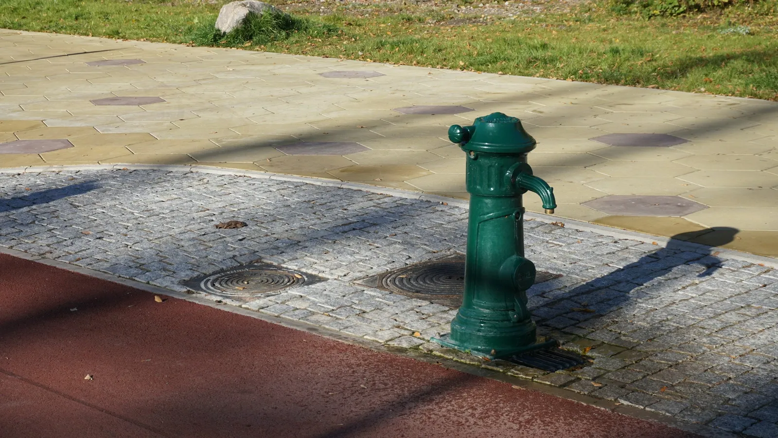 An old green street water pump on a pavement