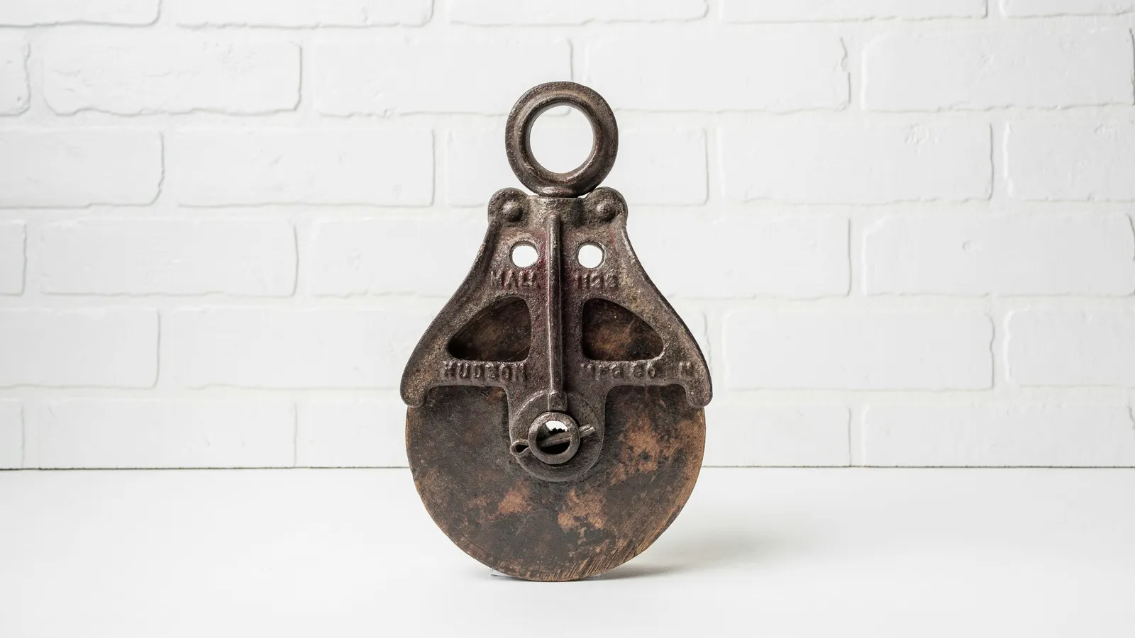 An old metal pulley block against a white brick wall
