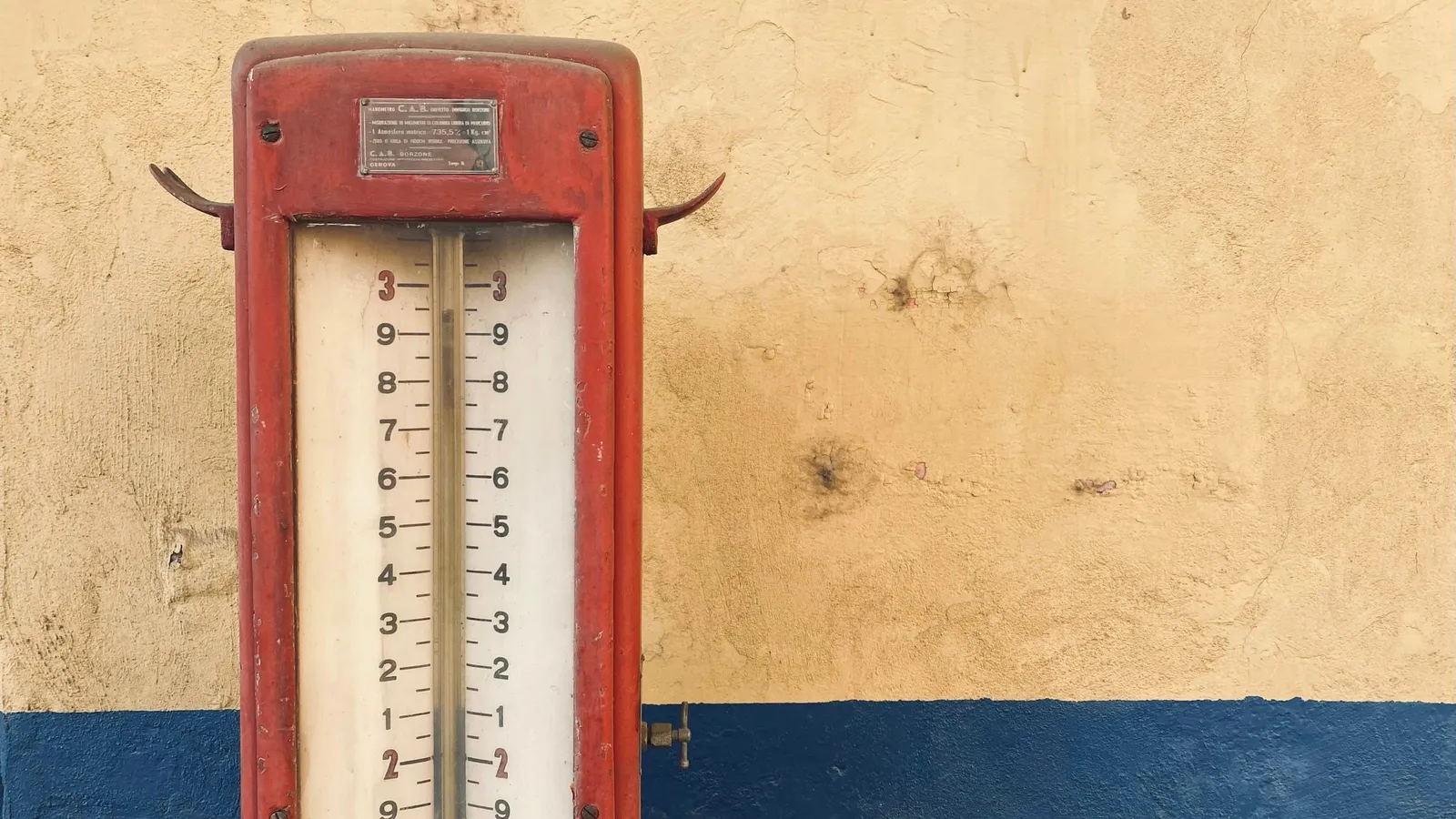 An old red wall thermometer with a printed scale