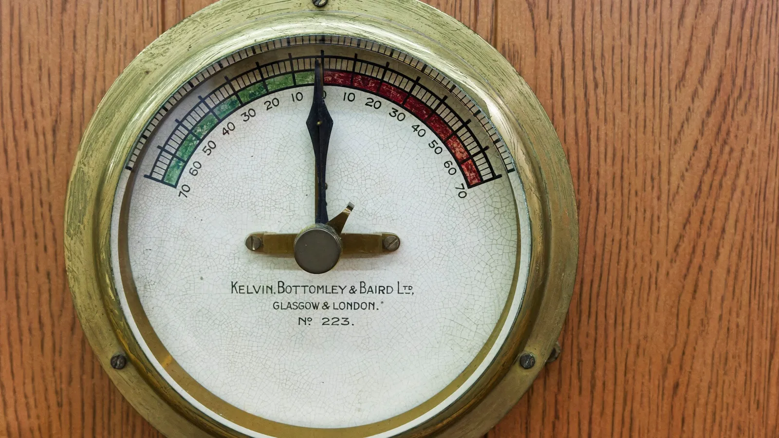 An old round gauge with a needle on a wooden wall
