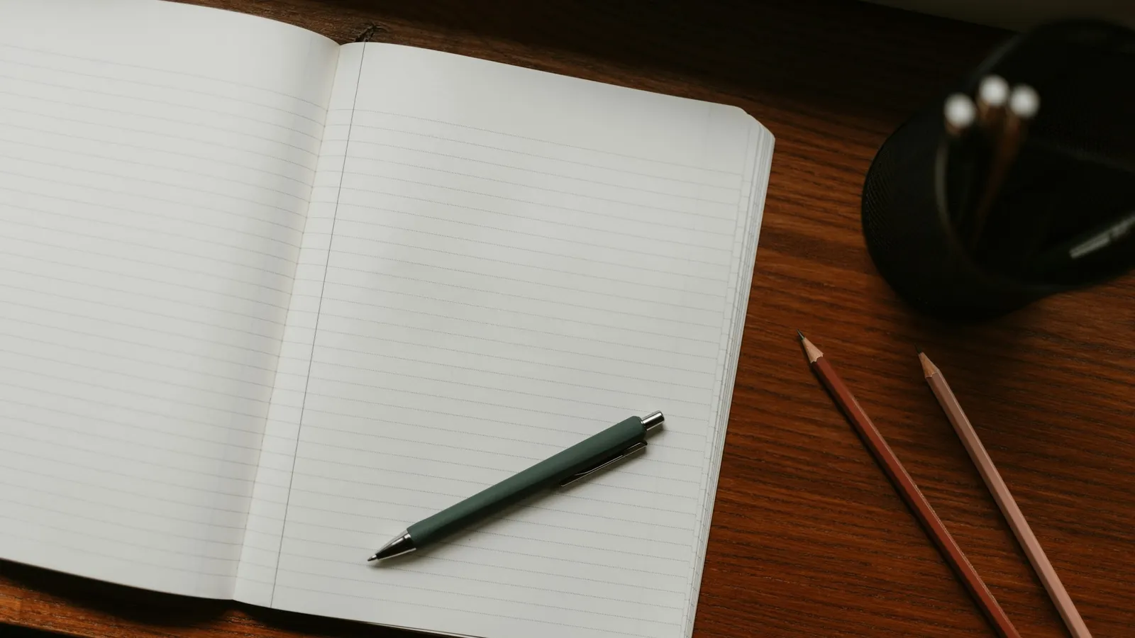 An open blank notebook with a pen and pencils on a desk