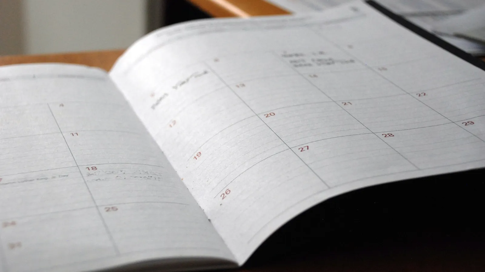 An open monthly planner lying on a wooden study desk