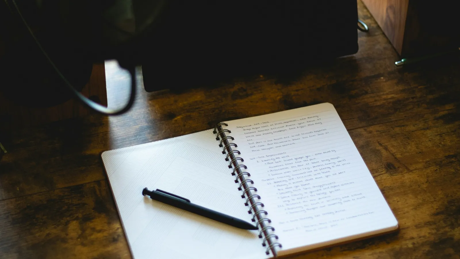 An open notebook and pen on a wooden desk
