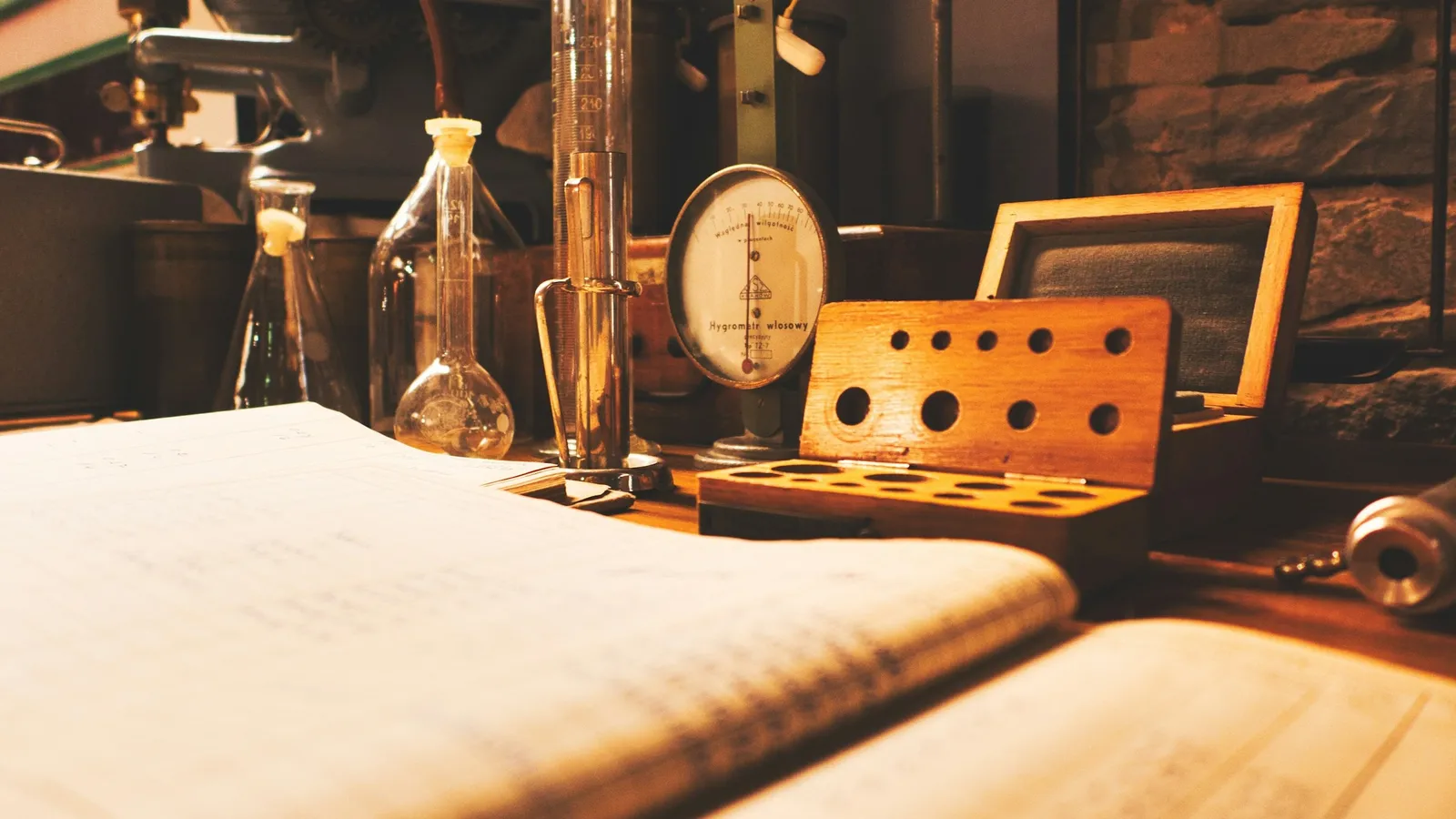 An open notebook beside old lab glassware on a wooden desk