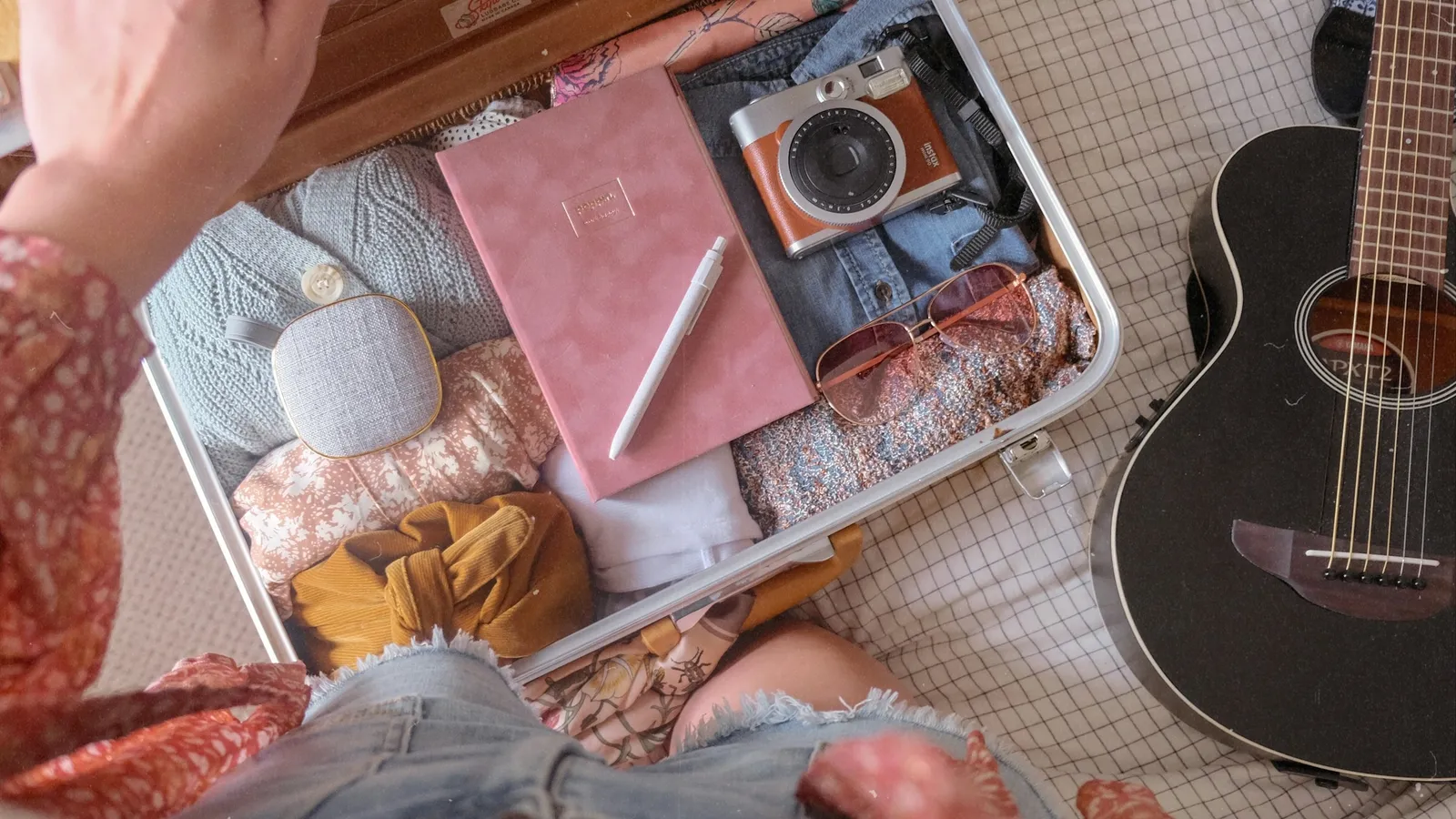 An open suitcase being packed with clothes, books and a notebook