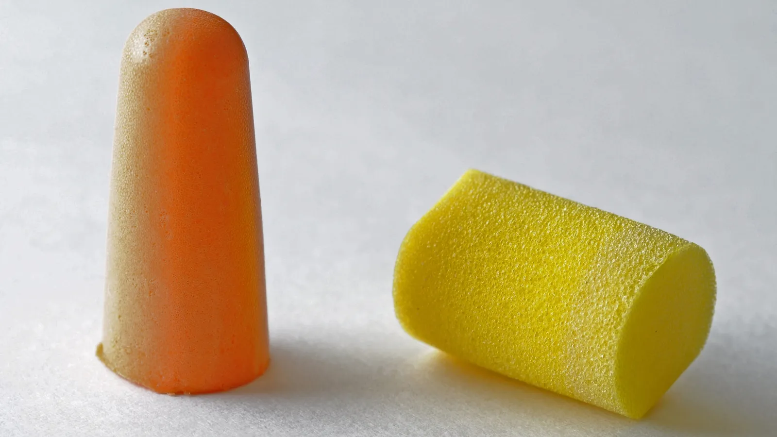 An orange and a yellow foam earplug on a white surface