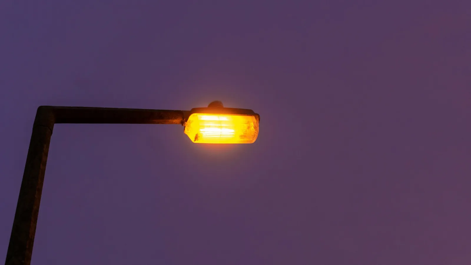 An orange sodium street lamp glowing at dusk