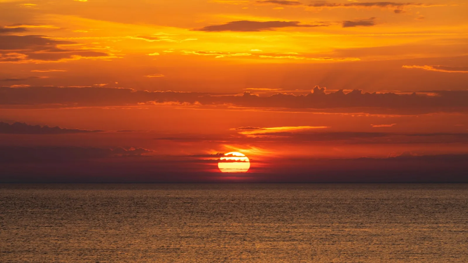 An orange Sun setting over a calm sea