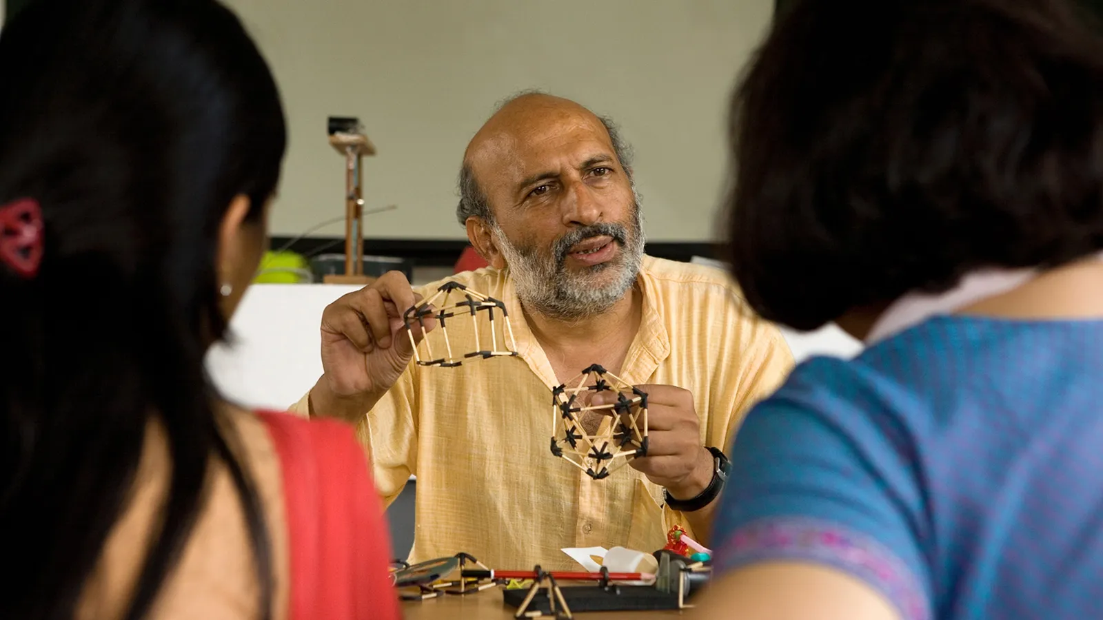 Arvind Gupta holding matchstick and rubber-joint models in front of two students