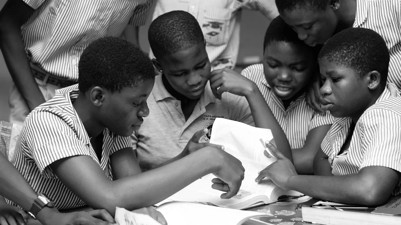 Black-and-white photo of uniformed school students leaning over open textbooks at a table
