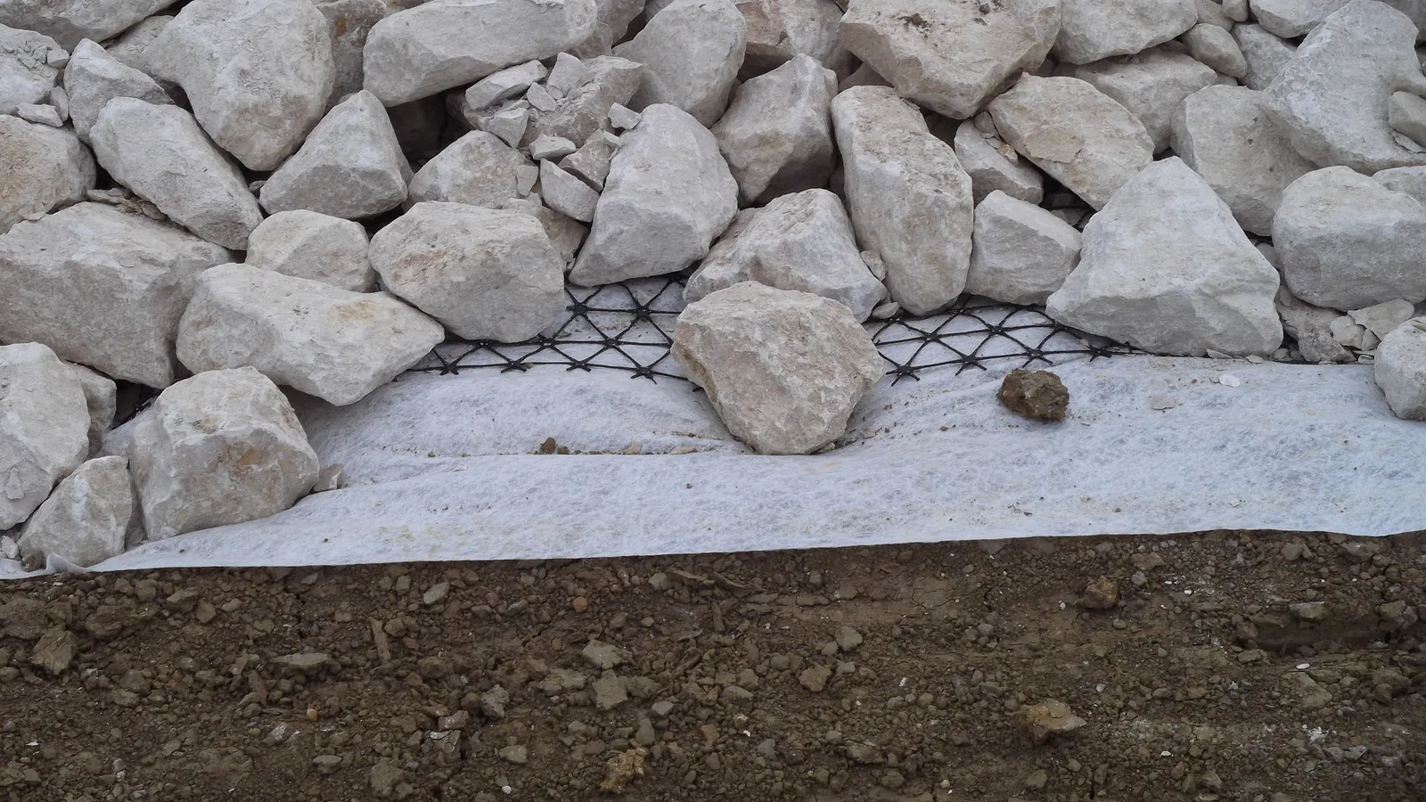 Black geogrid and white geotextile sheet laid between soil and rock fill