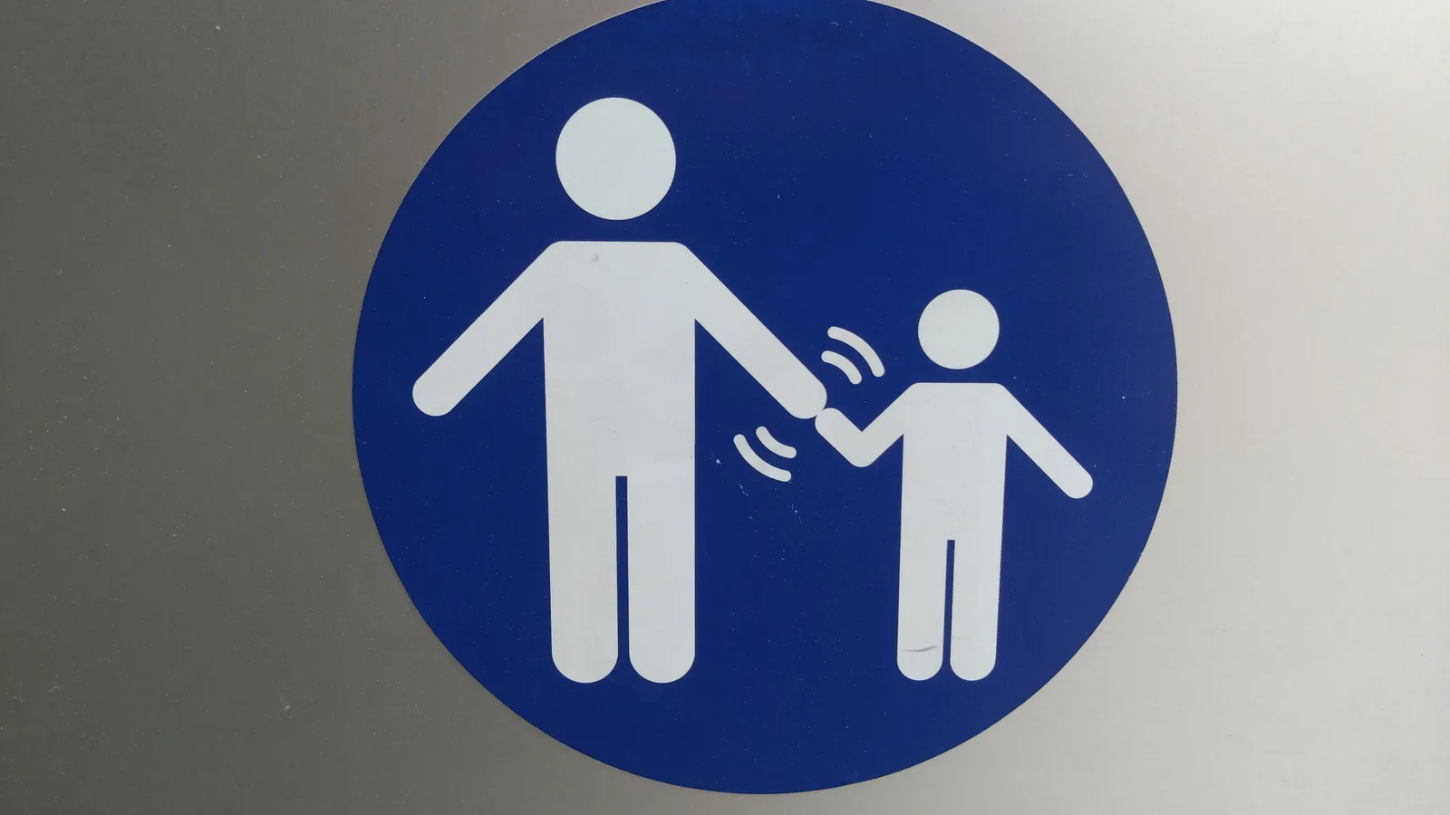 Blue round sign showing a white adult figure holding a small child's hand