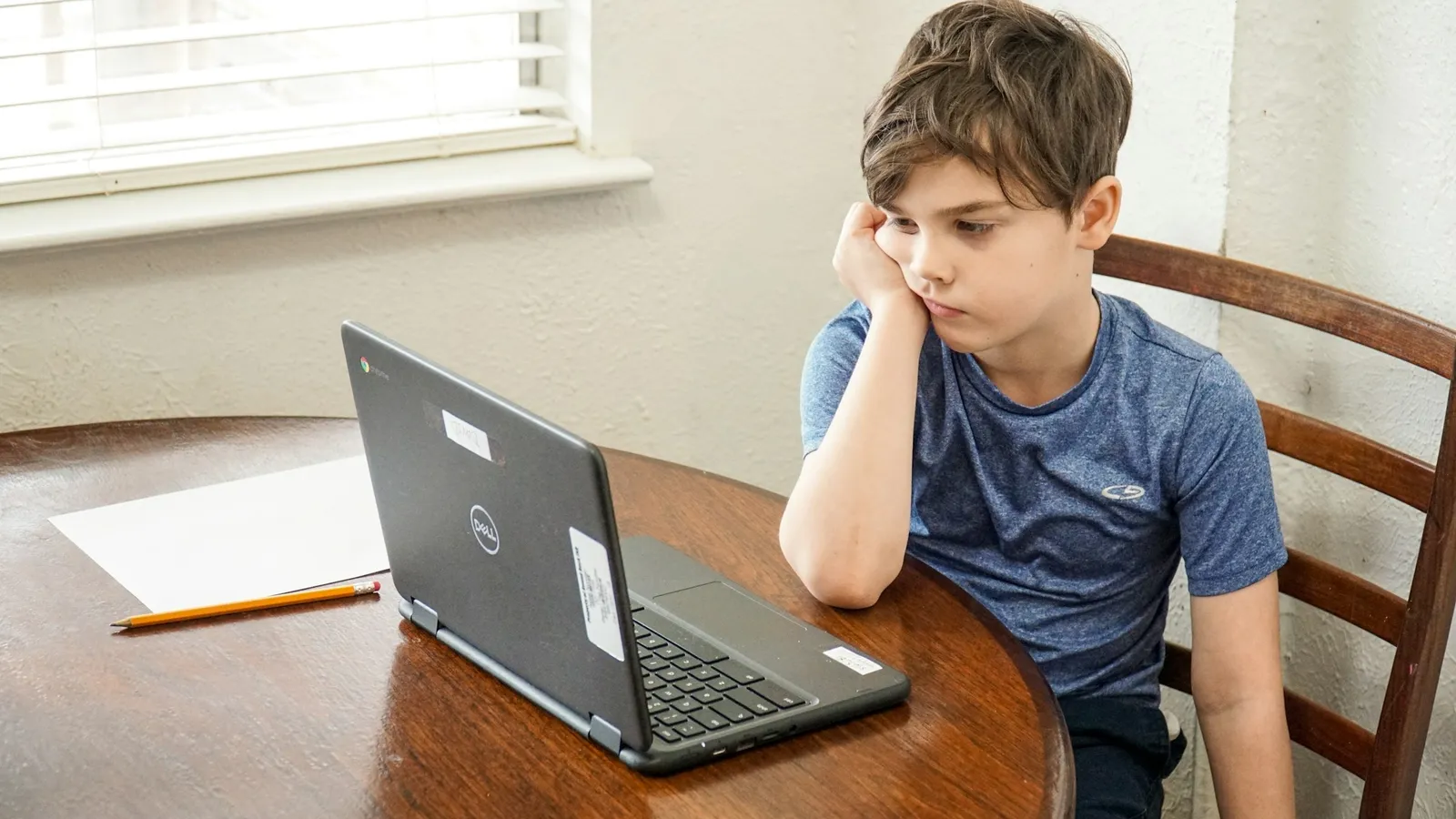 Boy resting his head on his hand in front of a laptop