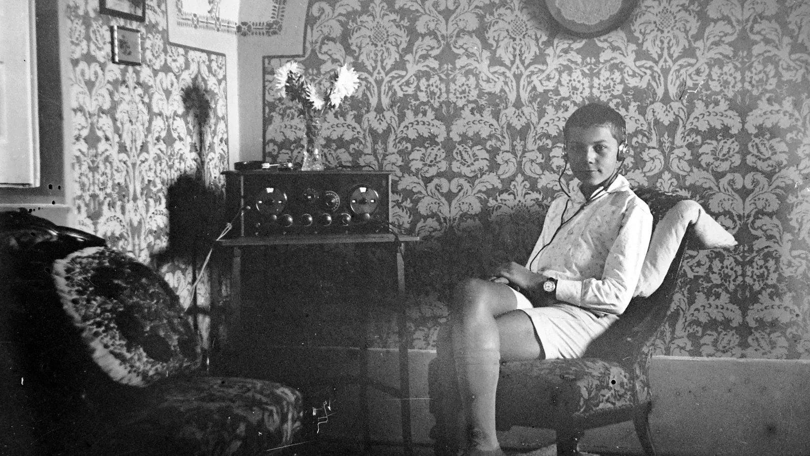 Boy wearing headphones sits in an armchair beside an old valve radio set