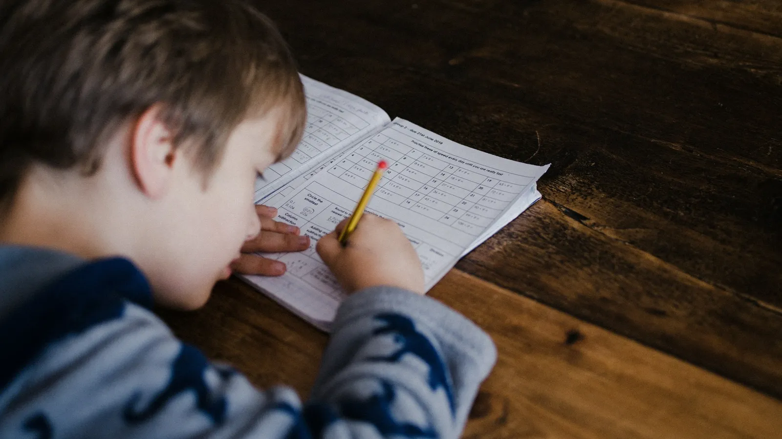 Boy writing out maths homework at a table