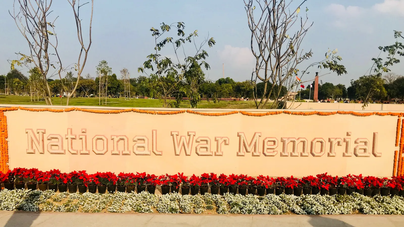 Carved National War Memorial sign in New Delhi lined with red poinsettias