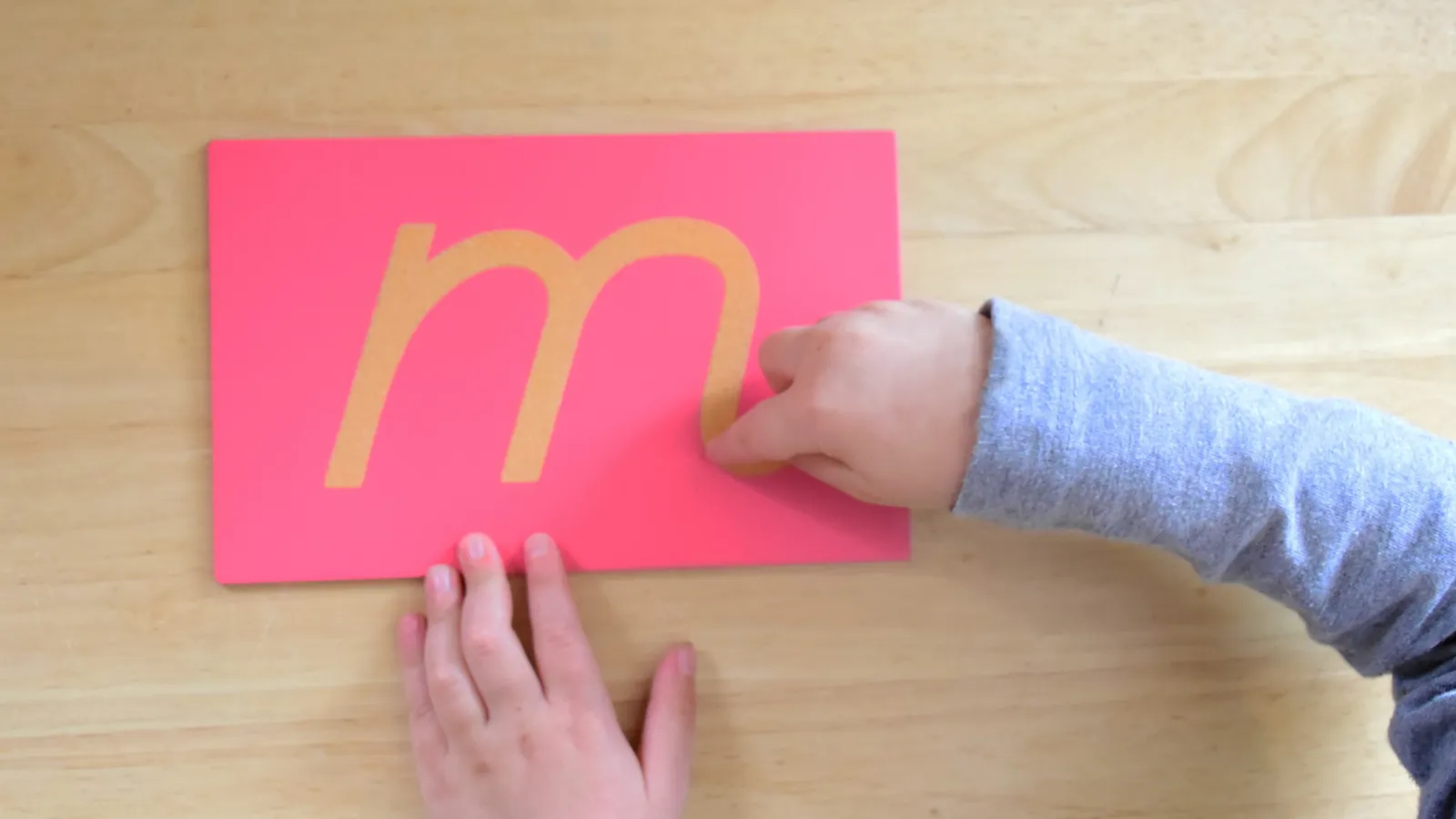 Child's finger tracing a sandpaper letter m on a pink card