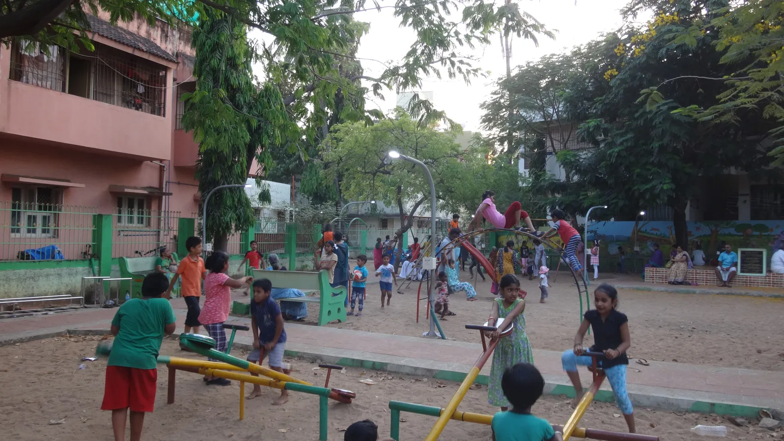 Children on seesaws and a climbing frame in a neighbourhood park beside apartment buildings