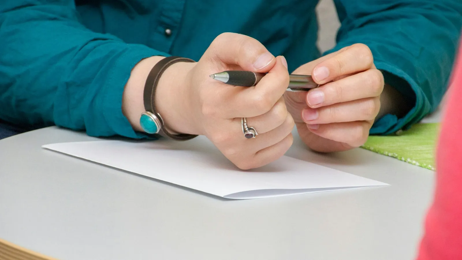 Clasped hands holding a pencil above a sheet of paper on a desk