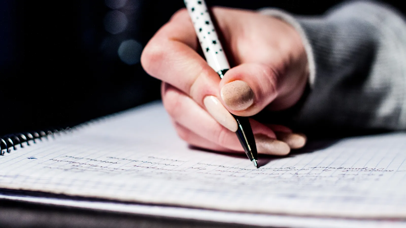 Close-up of a hand writing with a dotted pen in a spiral notebook