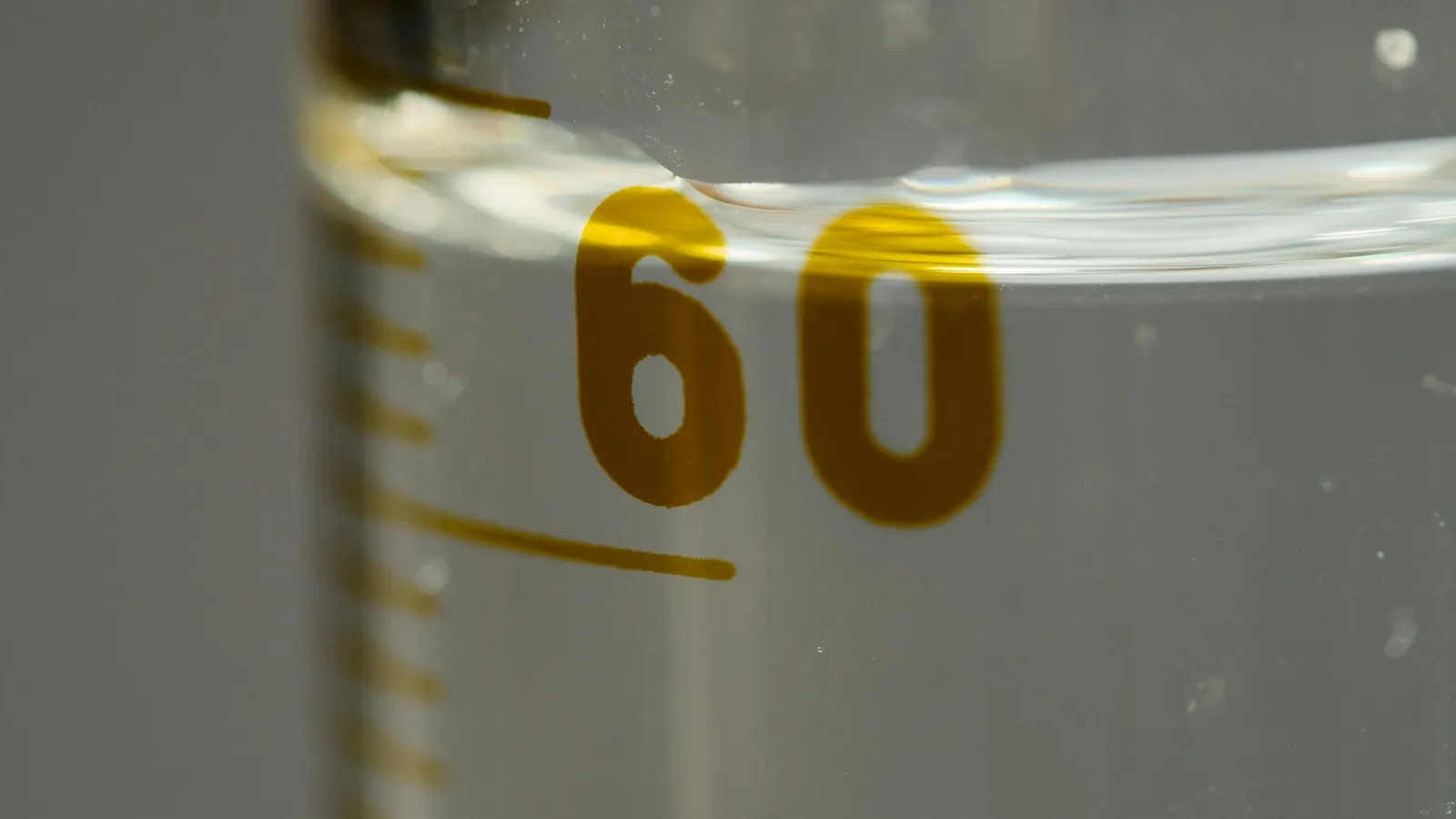 Close-up of the 60 mark on a measuring cylinder holding liquid
