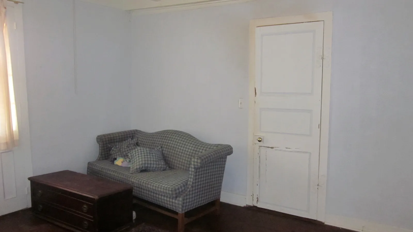 Closed white panelled door in a pale blue bedroom with a checked sofa and wooden chest