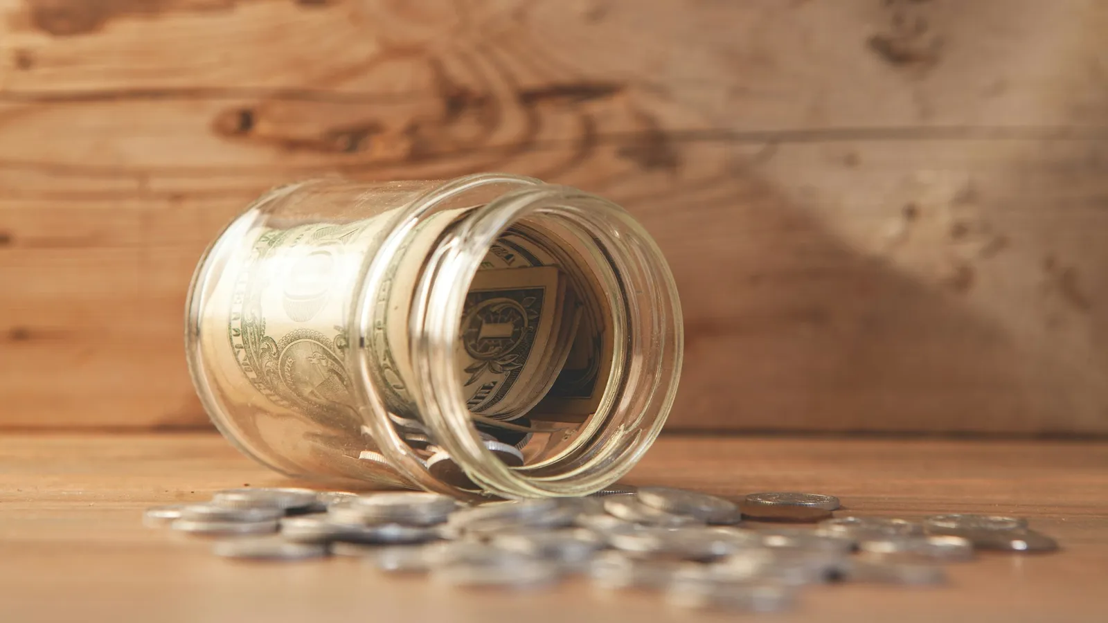 Coins spilling out of a glass jar onto a wooden table