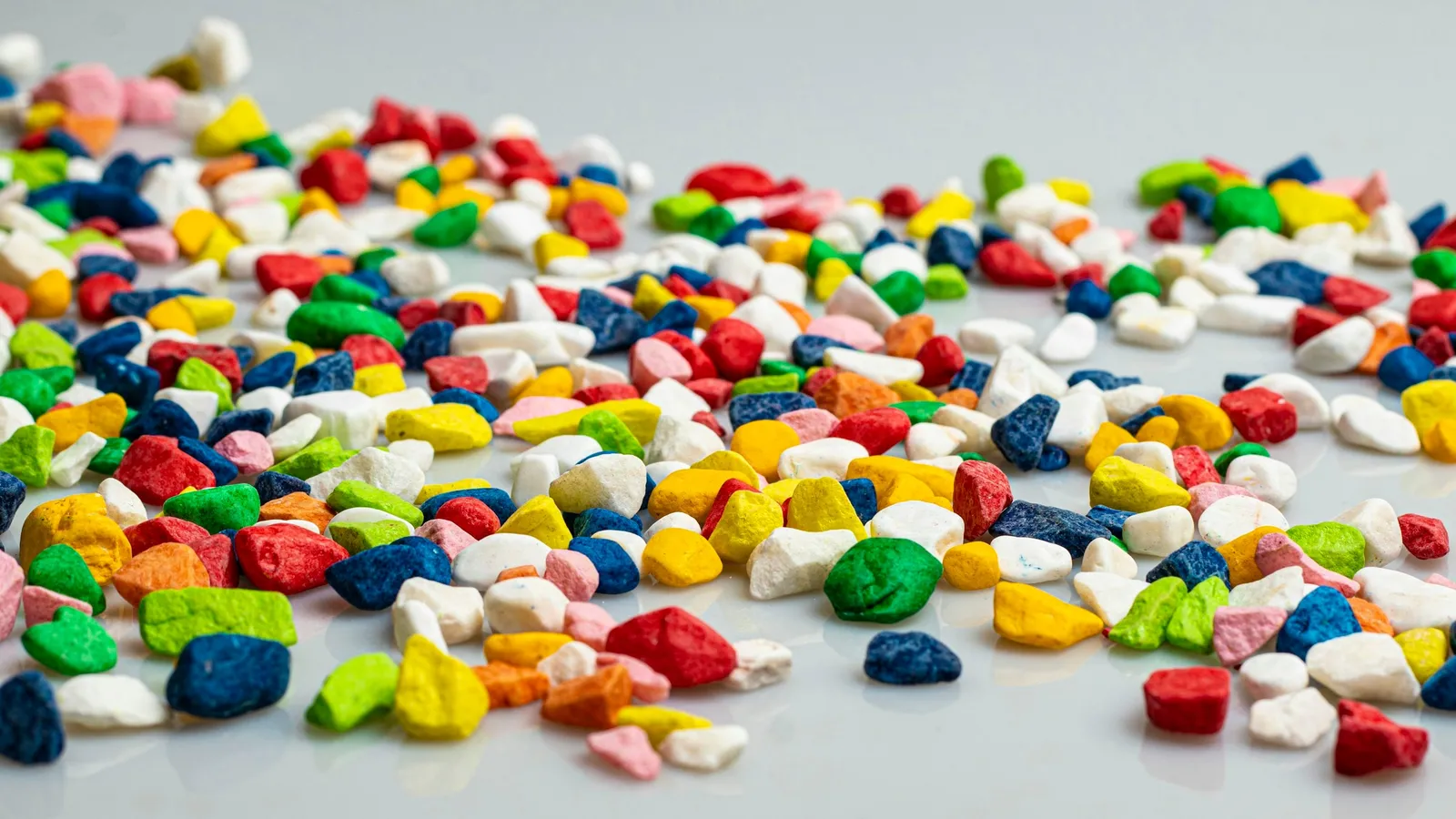 Colourful plastic pellets scattered on a white surface