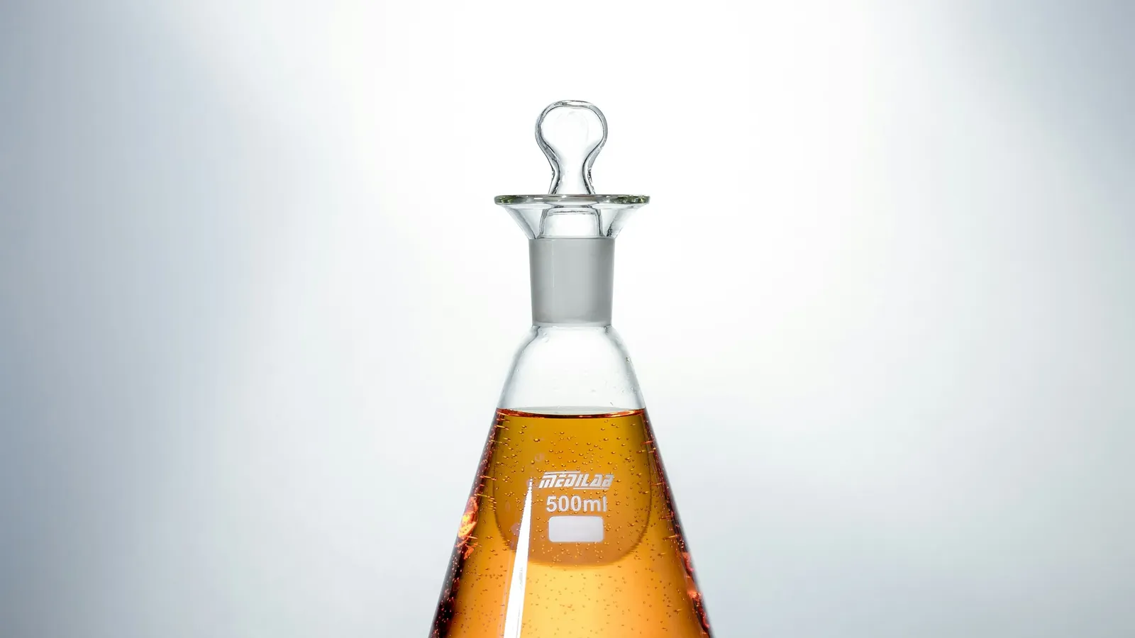 Conical flask filled with orange liquid against a white background