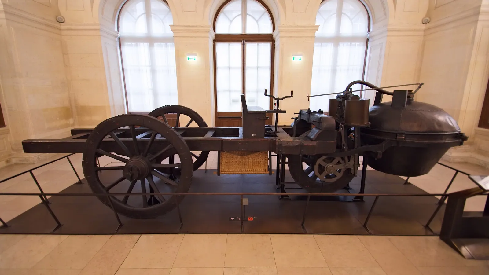 Cugnot's wooden steam cart in a Paris museum, its large round boiler overhanging the single front wheel
