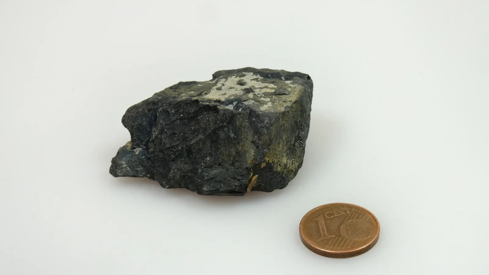 Dark columbite mineral specimen beside a one euro cent coin for scale
