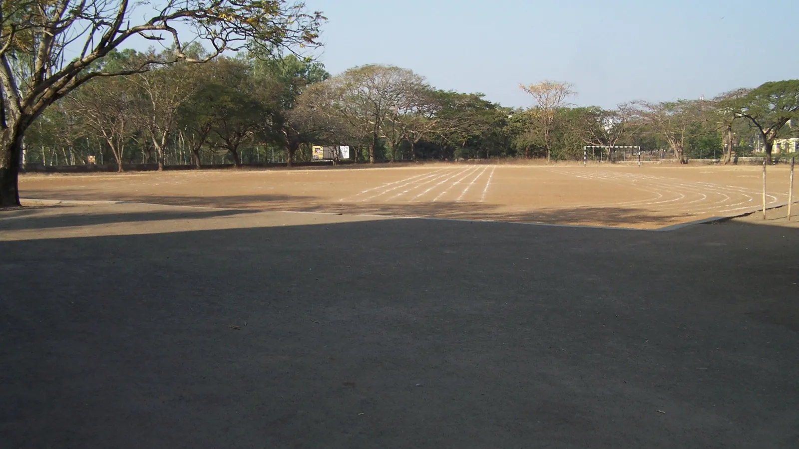 Dirt school sports ground in India with a chalk-marked running track and a goal