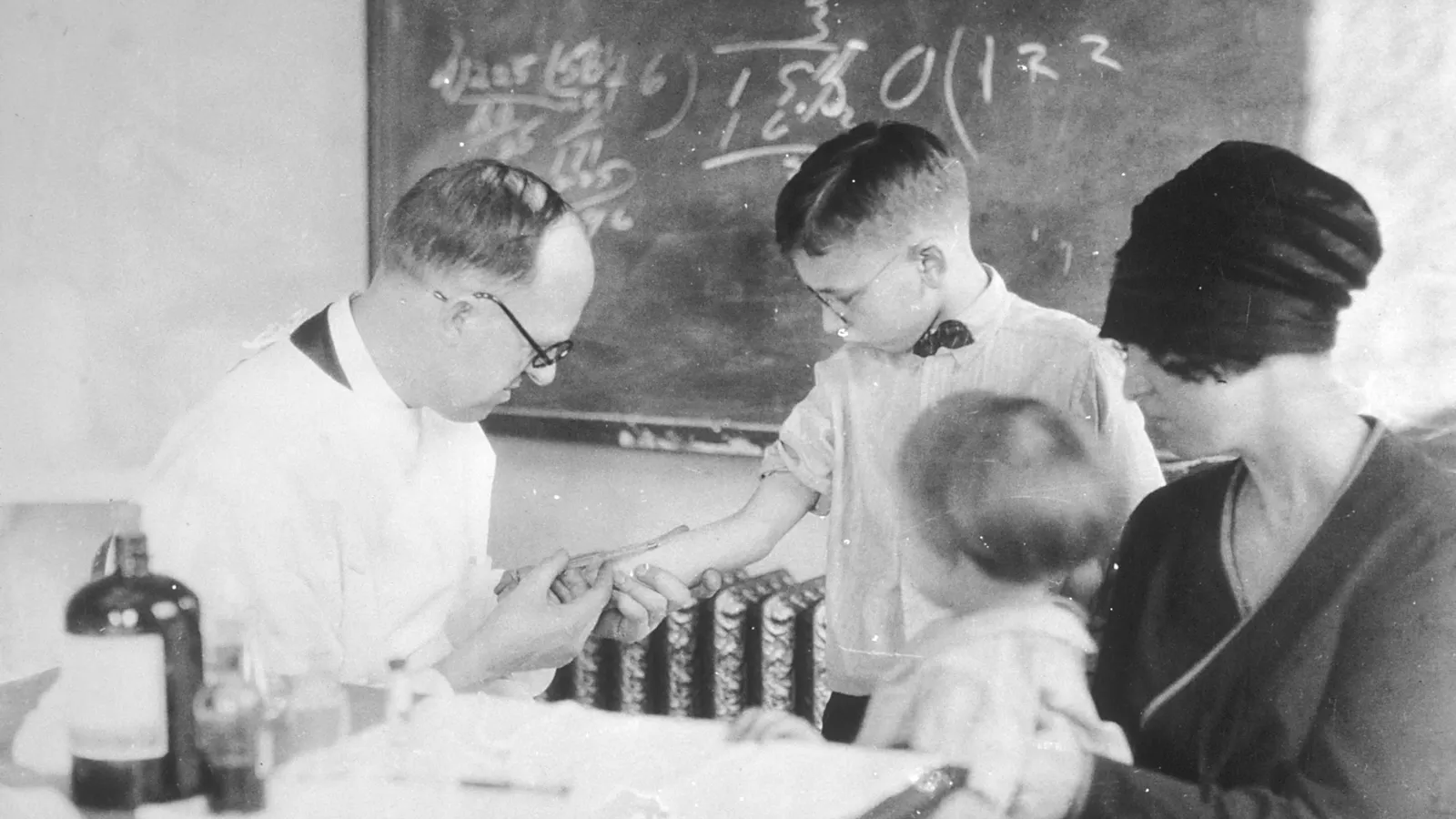 Doctor gives a boy a Schick skin test while his mother and baby sibling watch