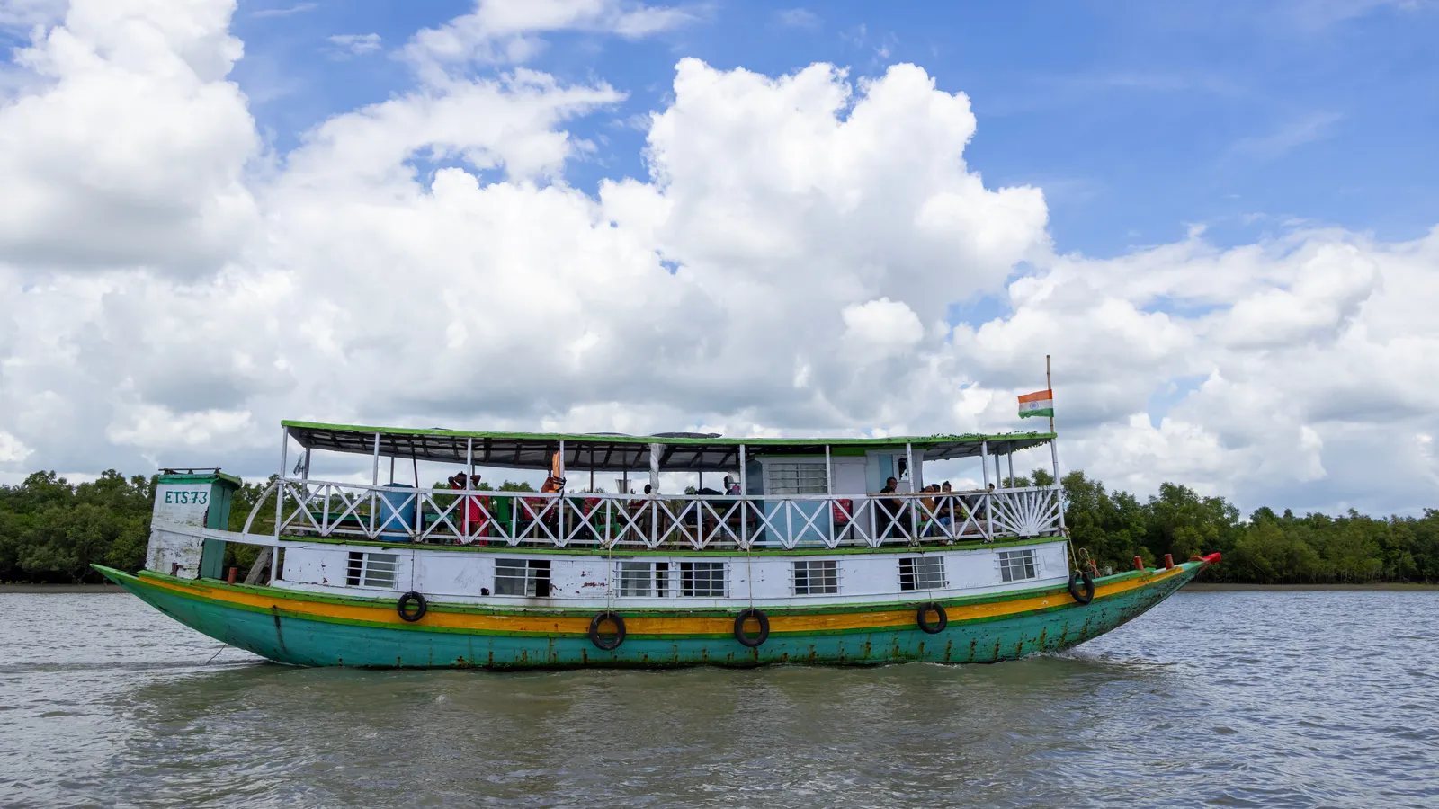Double-deck tourist boat with visitors on its upper deck, on a river lined with mangroves in the Sundarbans