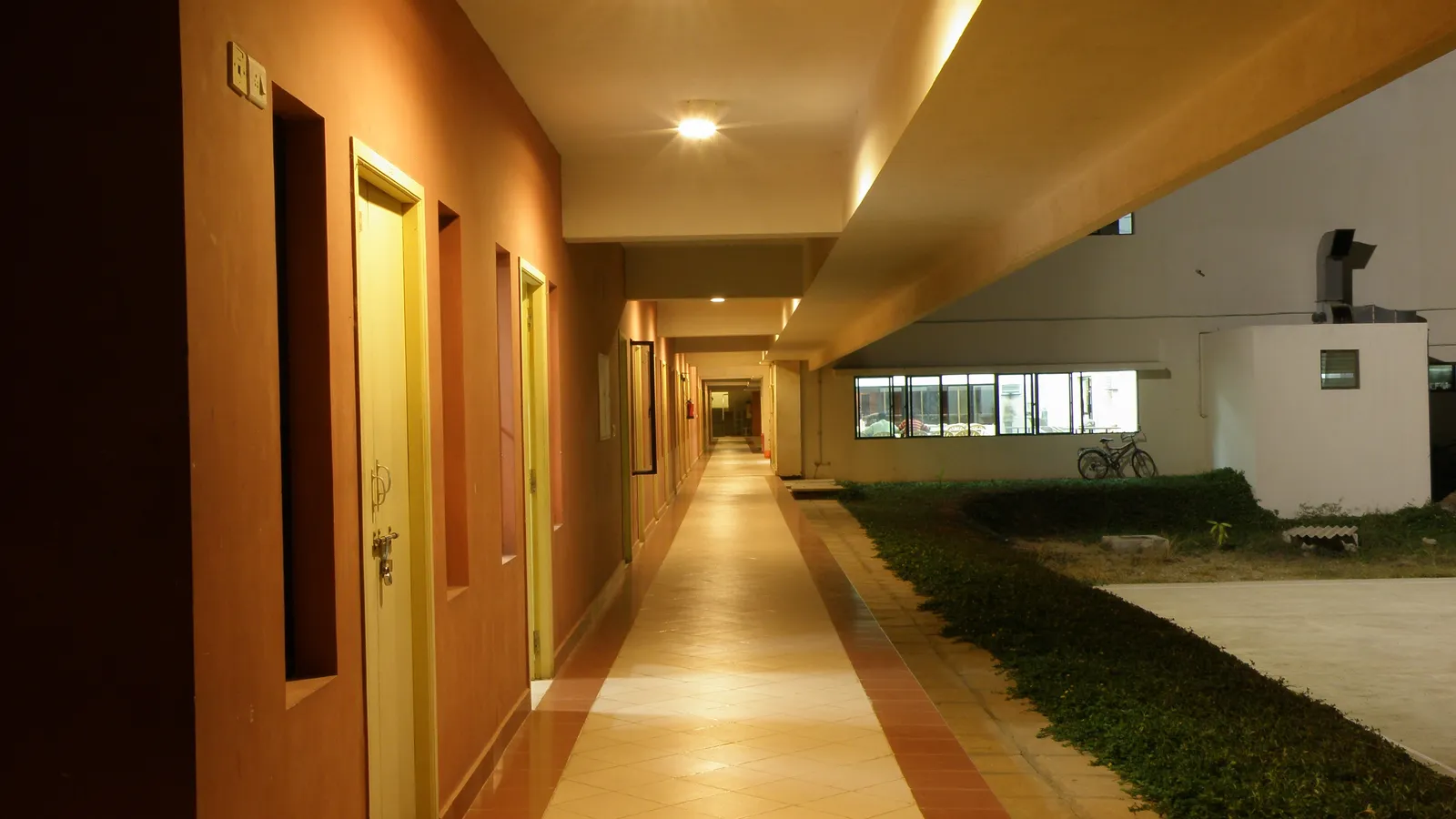 Empty, brightly lit college hostel corridor with closed room doors at night