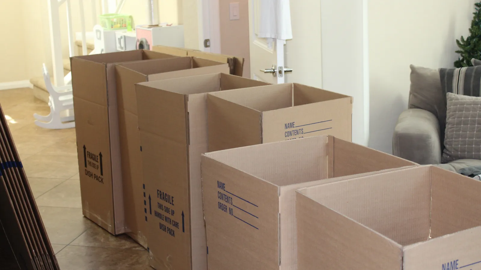 Empty cardboard moving boxes lined up in a living room near a staircase