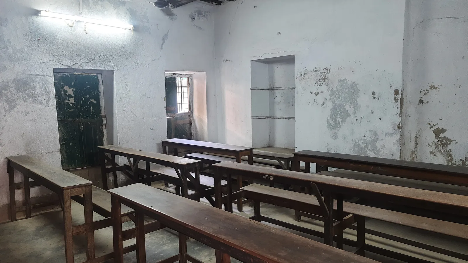 Empty classroom with rows of long wooden benches and desks