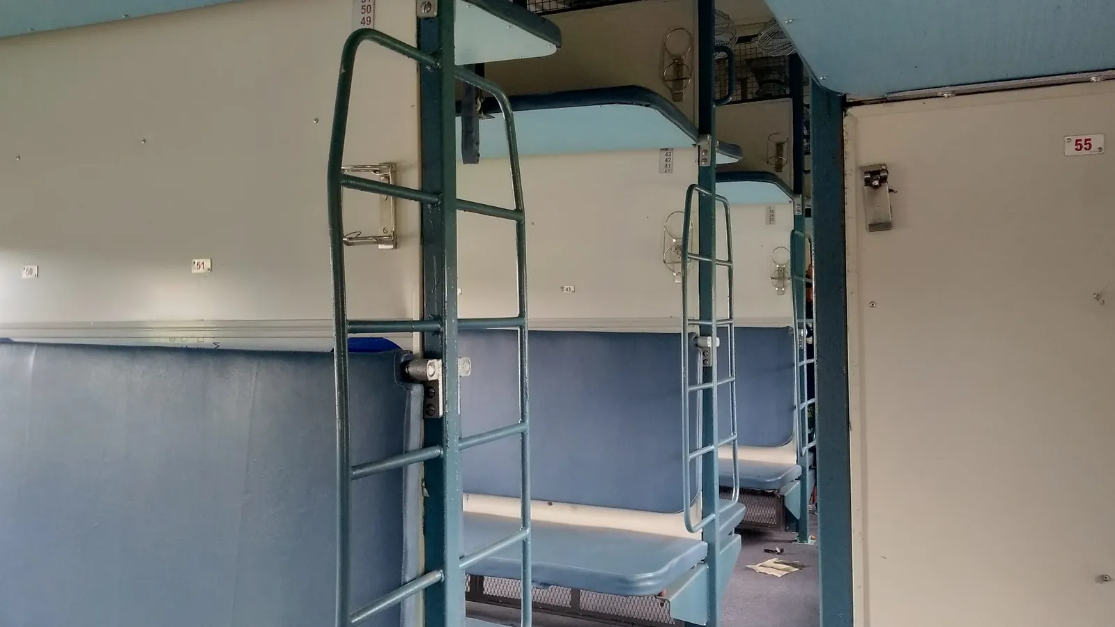 Empty Indian Railways sleeper coach with blue berths and metal ladders