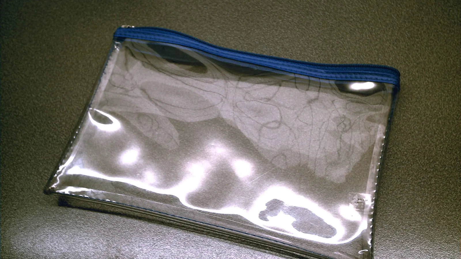 Empty transparent zip pouch with a blue zip on a dark desk