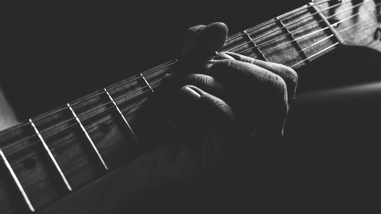 Fingers pressing the strings of a guitar, in black and white