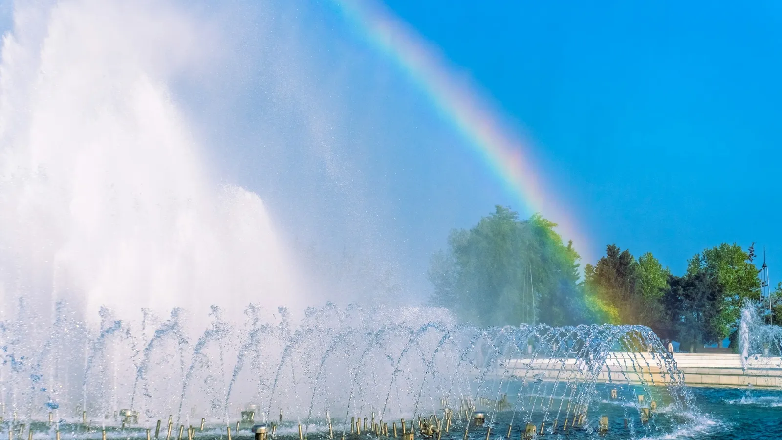 Fountain jets of water arcing through the air with a rainbow behind