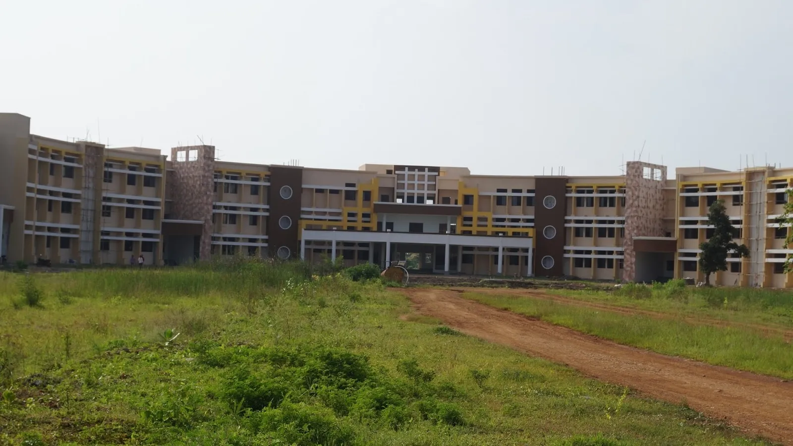 Four-storey college building beyond a grassy field and a dirt track