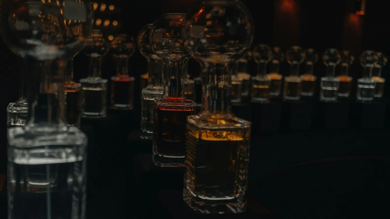 Glass bottles of clear and amber liquids in dim light