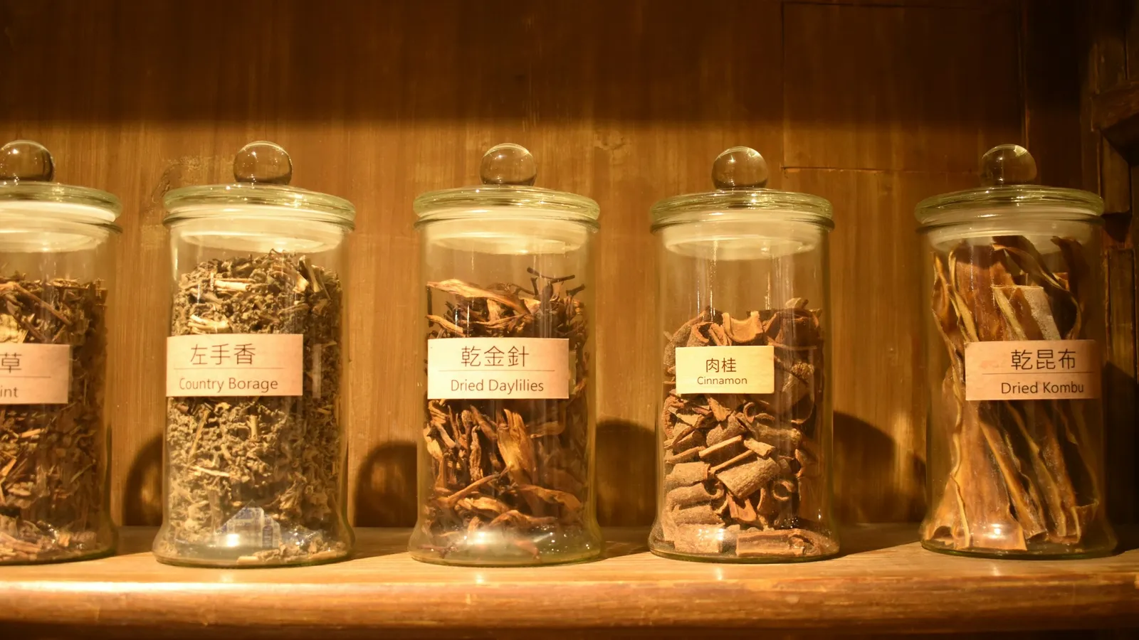 Glass jars of dried herbs lined up on a wooden shelf