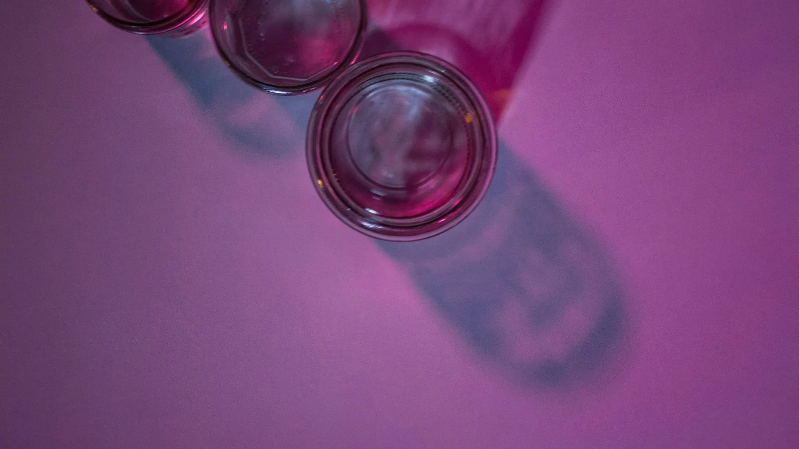 Glass vials of pink liquid seen from above on a purple surface