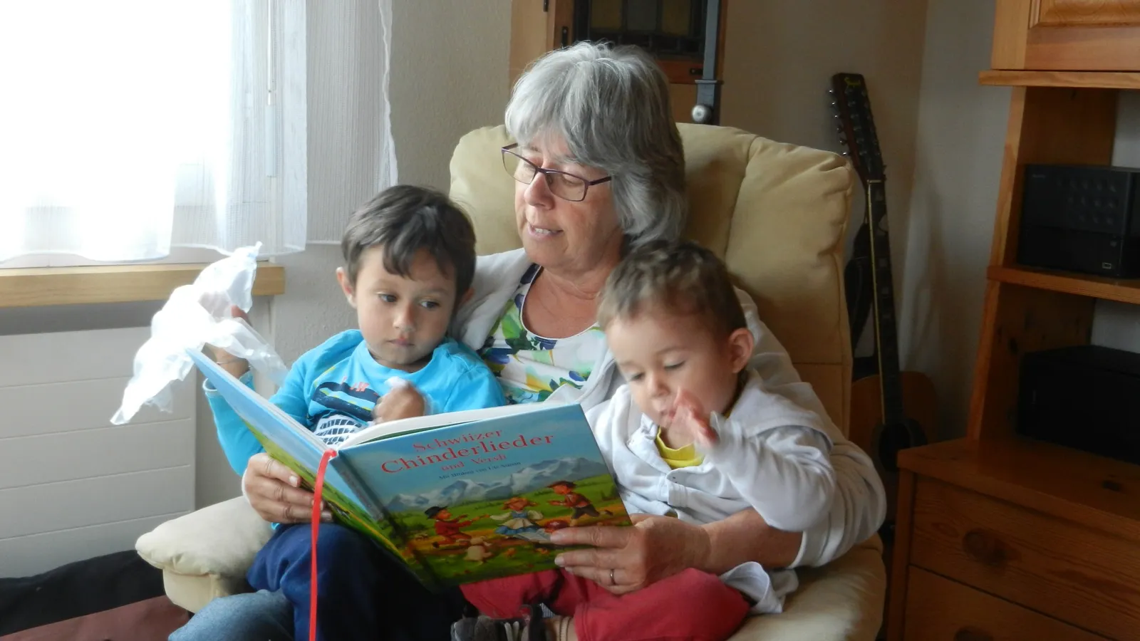 Grandmother in an armchair reading a picture book to two young grandsons