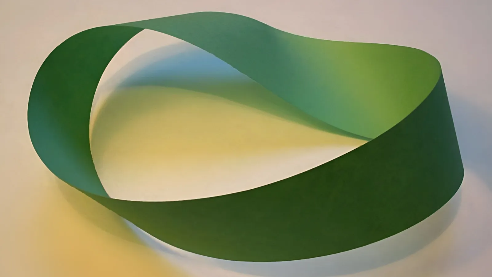 Green paper Möbius strip with a single half-twist resting on white paper